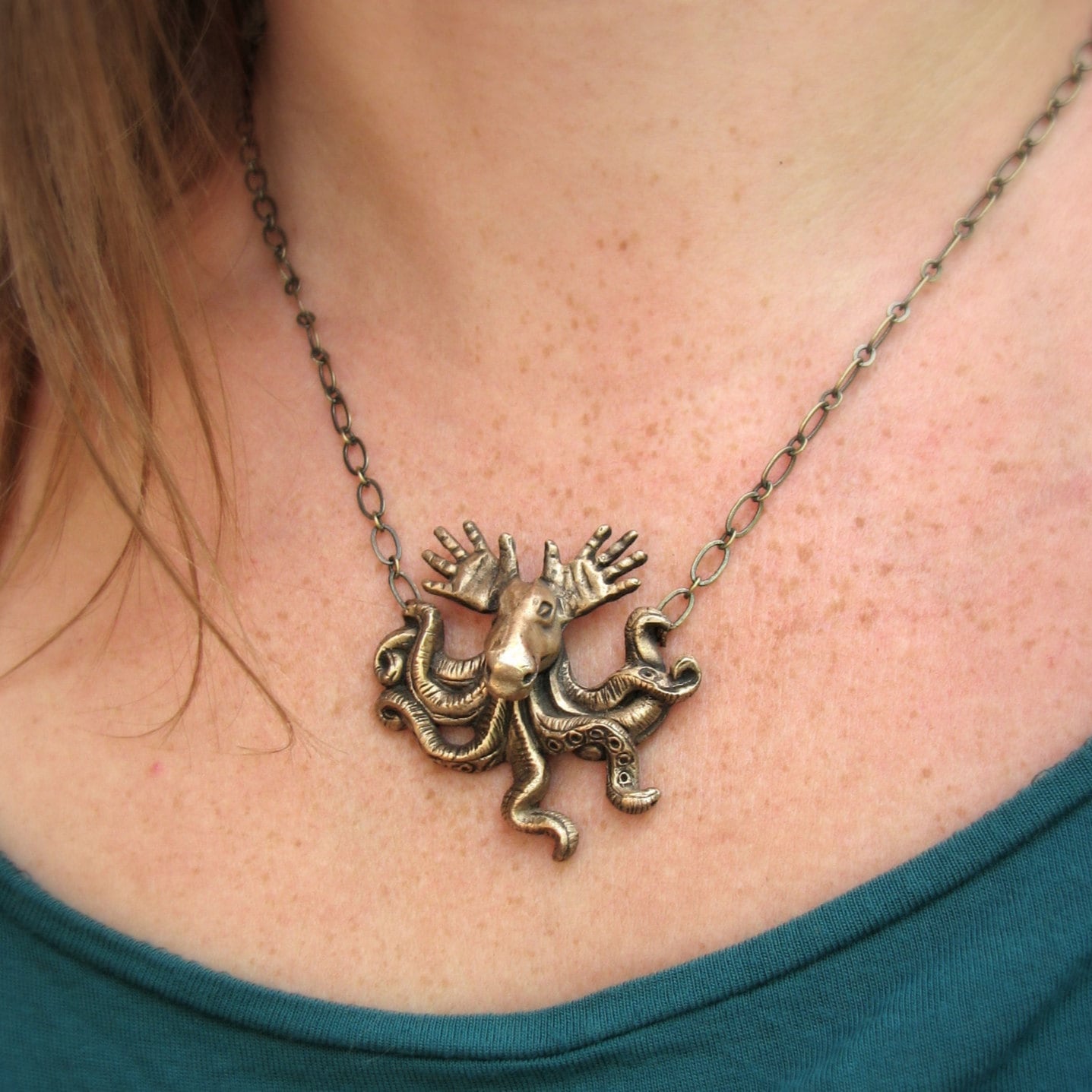 A bronze pendant featuring a surreal creature with tentacles and antlers, resembling a moose with hands as antlers