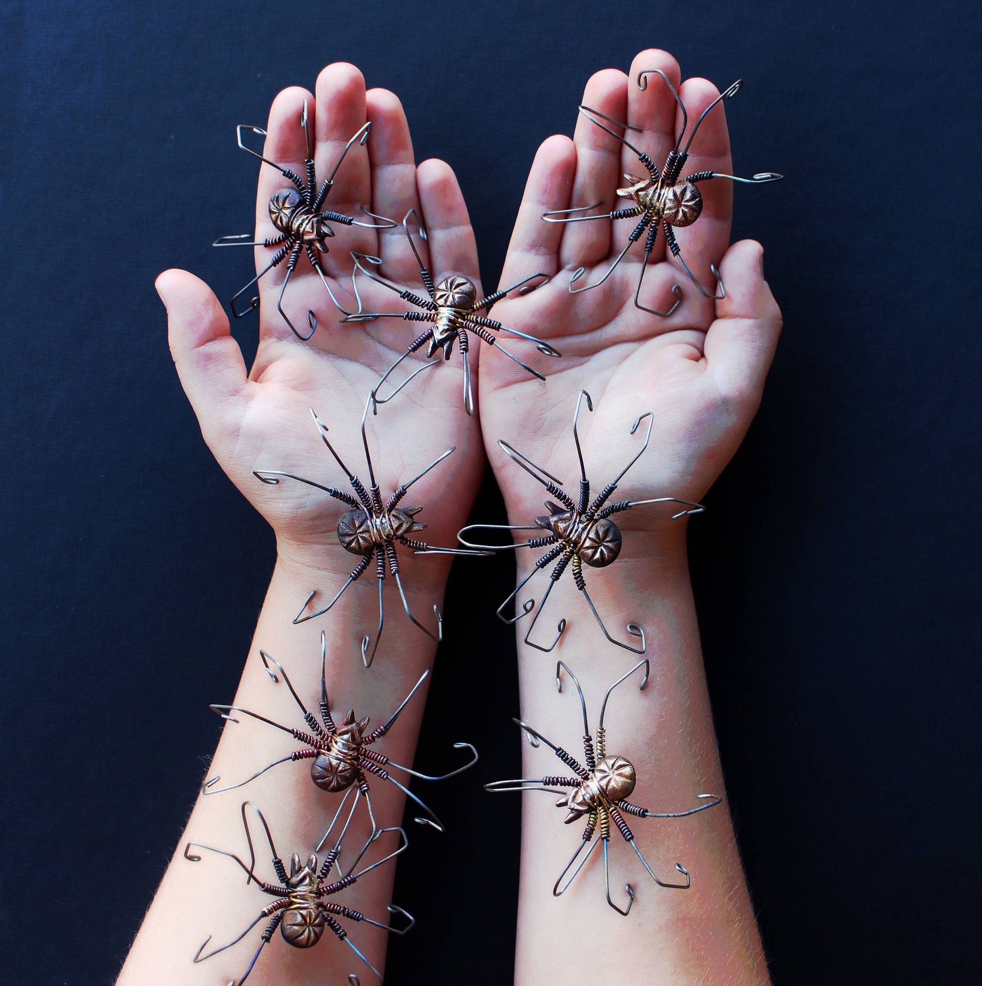 wire wrapped spiders crawling on a persons arms