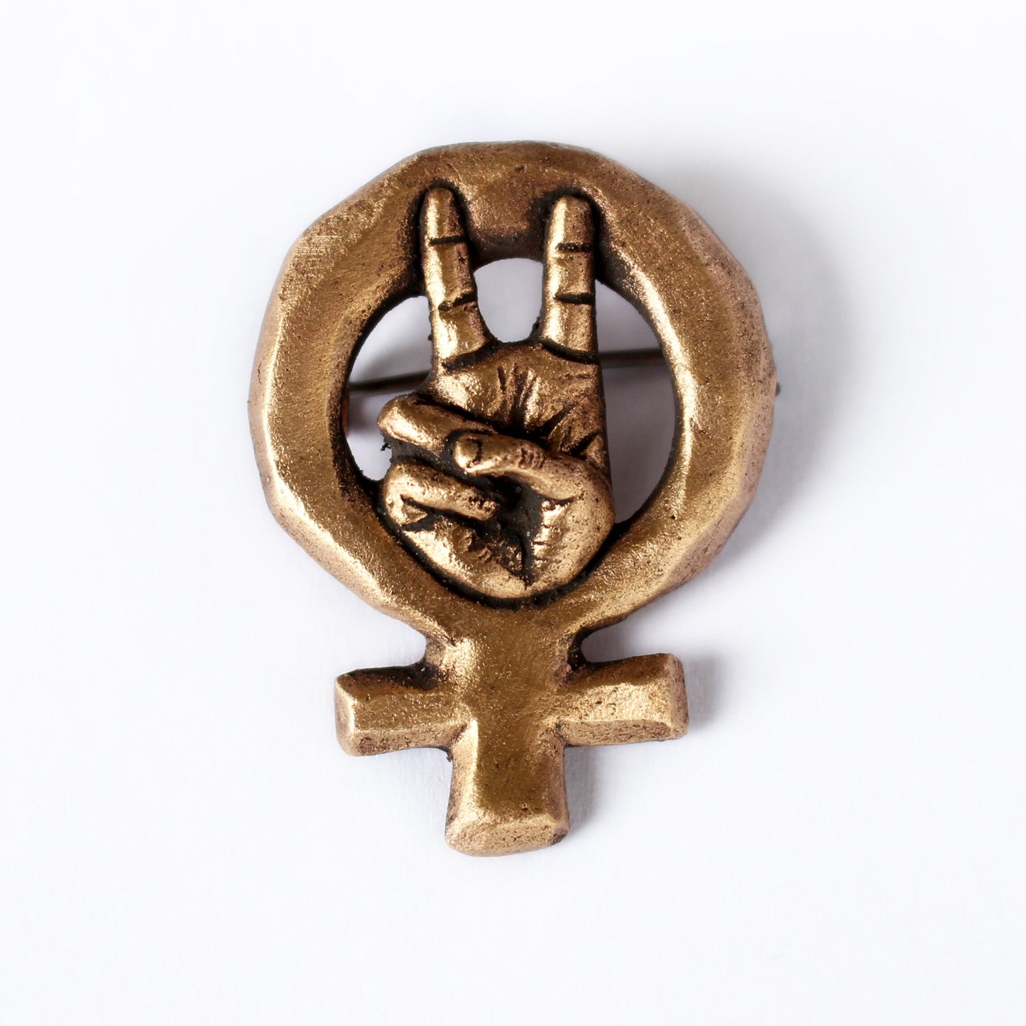 A bronze brooch with a miniature hand signaling victory framed by the Venus symbol, mounted on a white background.