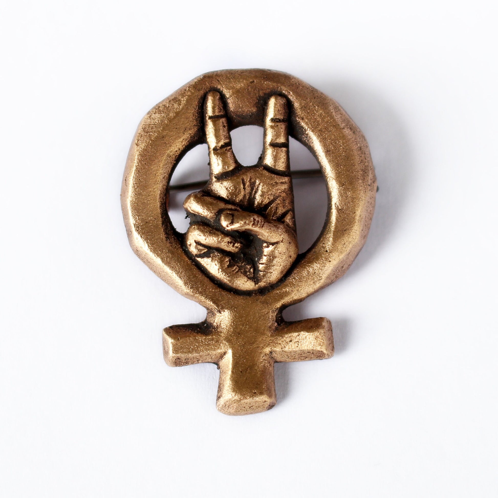 A bronze brooch with a miniature hand signaling victory framed by the Venus symbol, mounted on a white background.