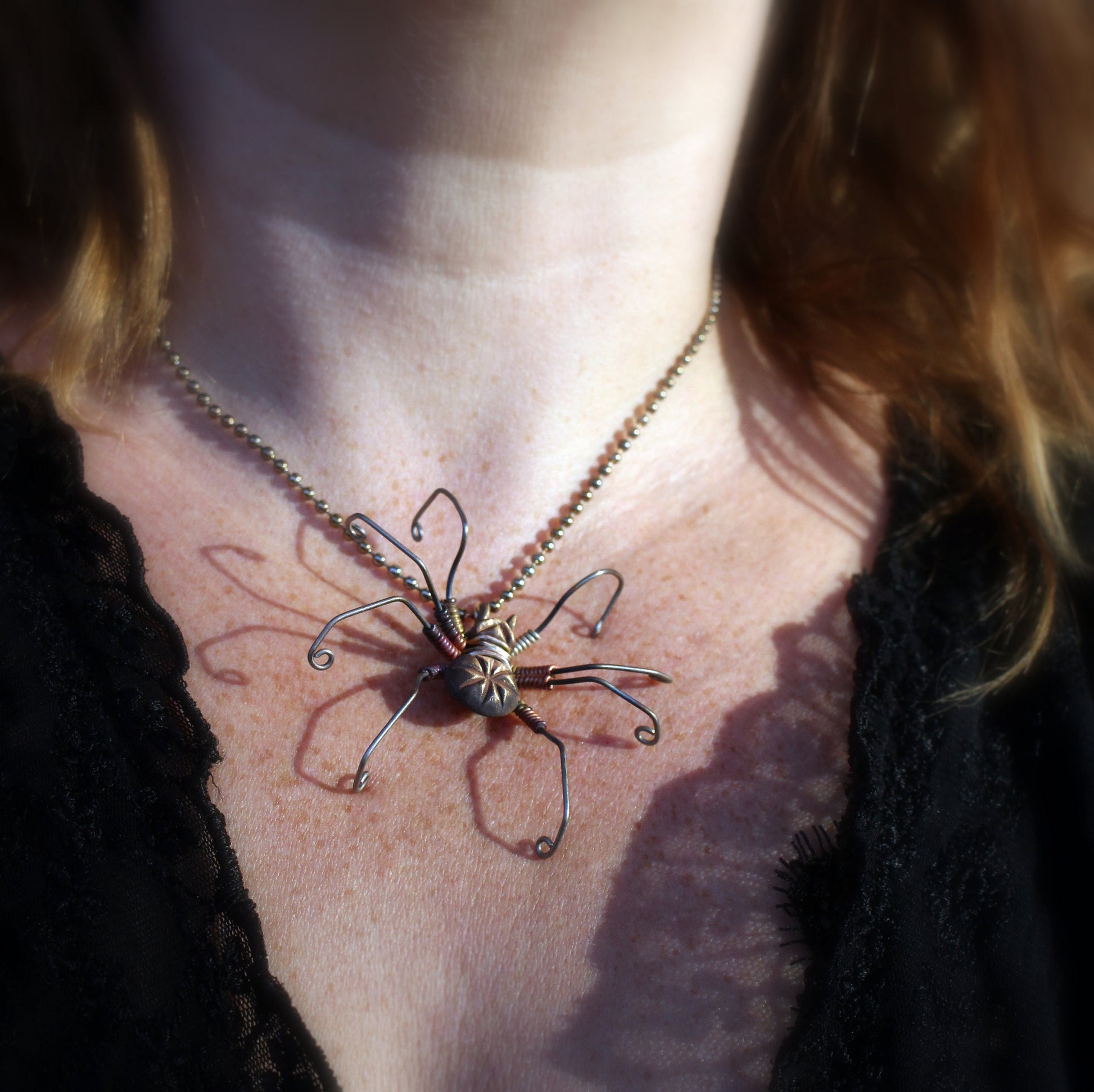 A person wearing a necklace with a large, detailed spider pendant made of bronze with oxidized dark and polished details.