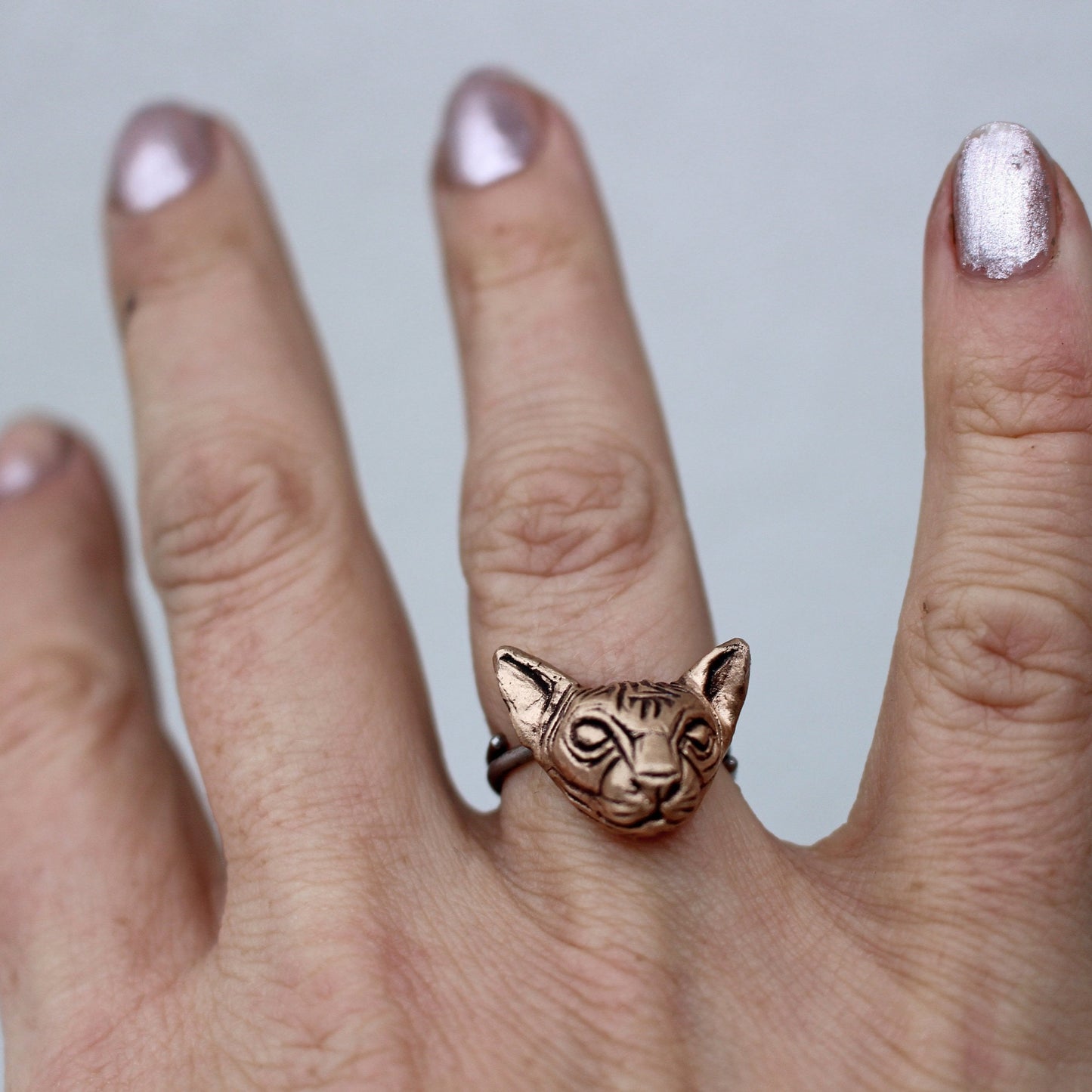 A bronze-colored hairless cat head ring on a person's finger, with the ring band visible.