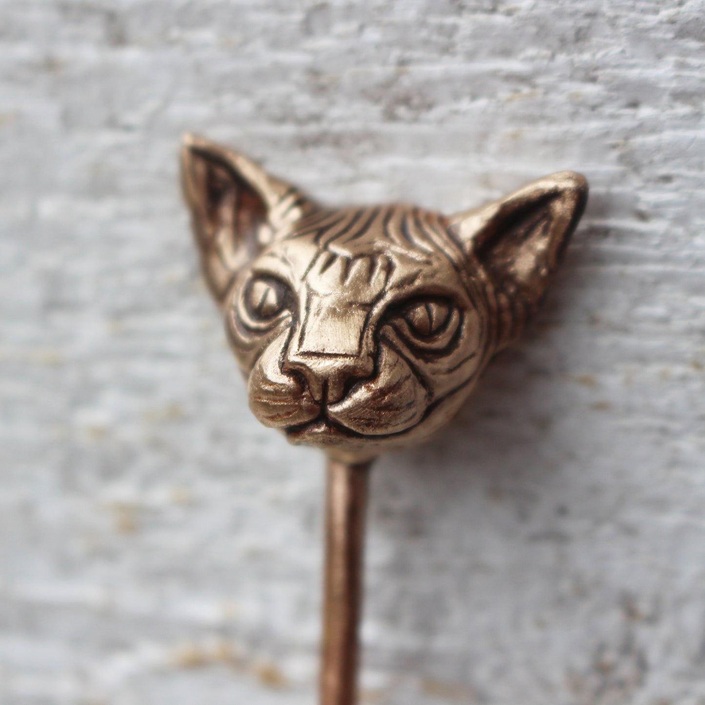 A bronze hair stick with a sculpted face of a Sphynx cat at the top