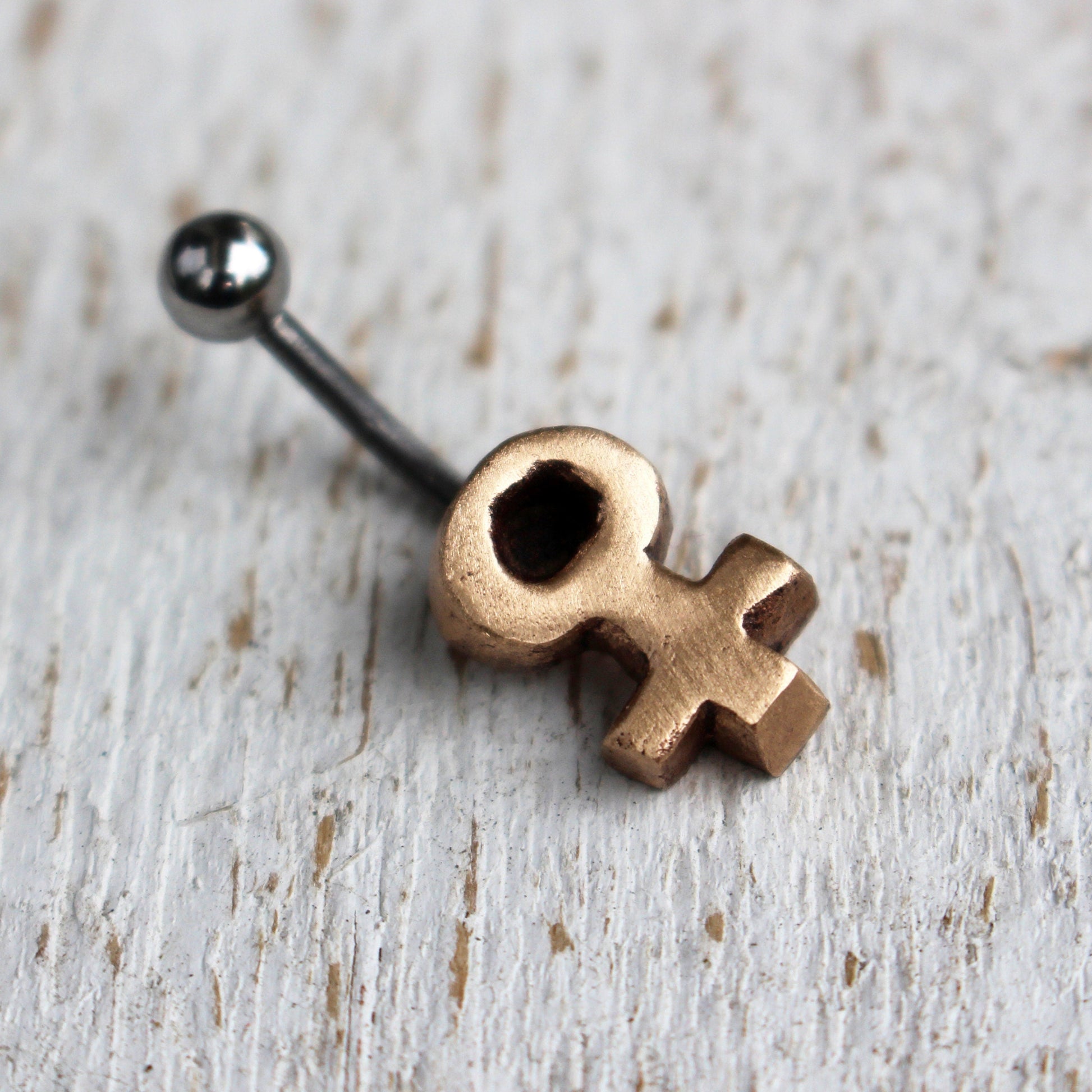 A belly button ring with a small bronze Venus symbol attached to one end of a curved barbell.