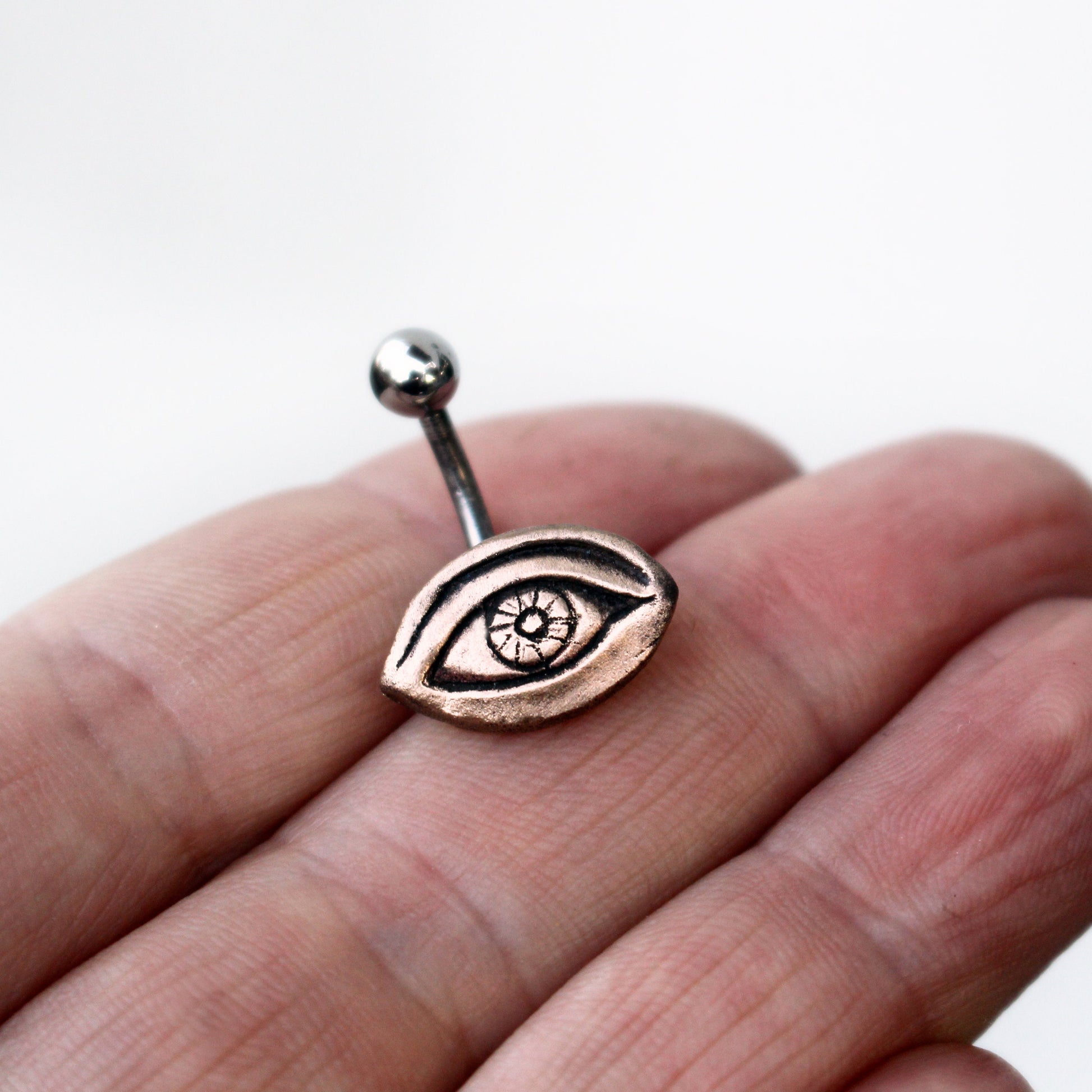 A belly button ring with a bronze eye design attached to a curved barbell.