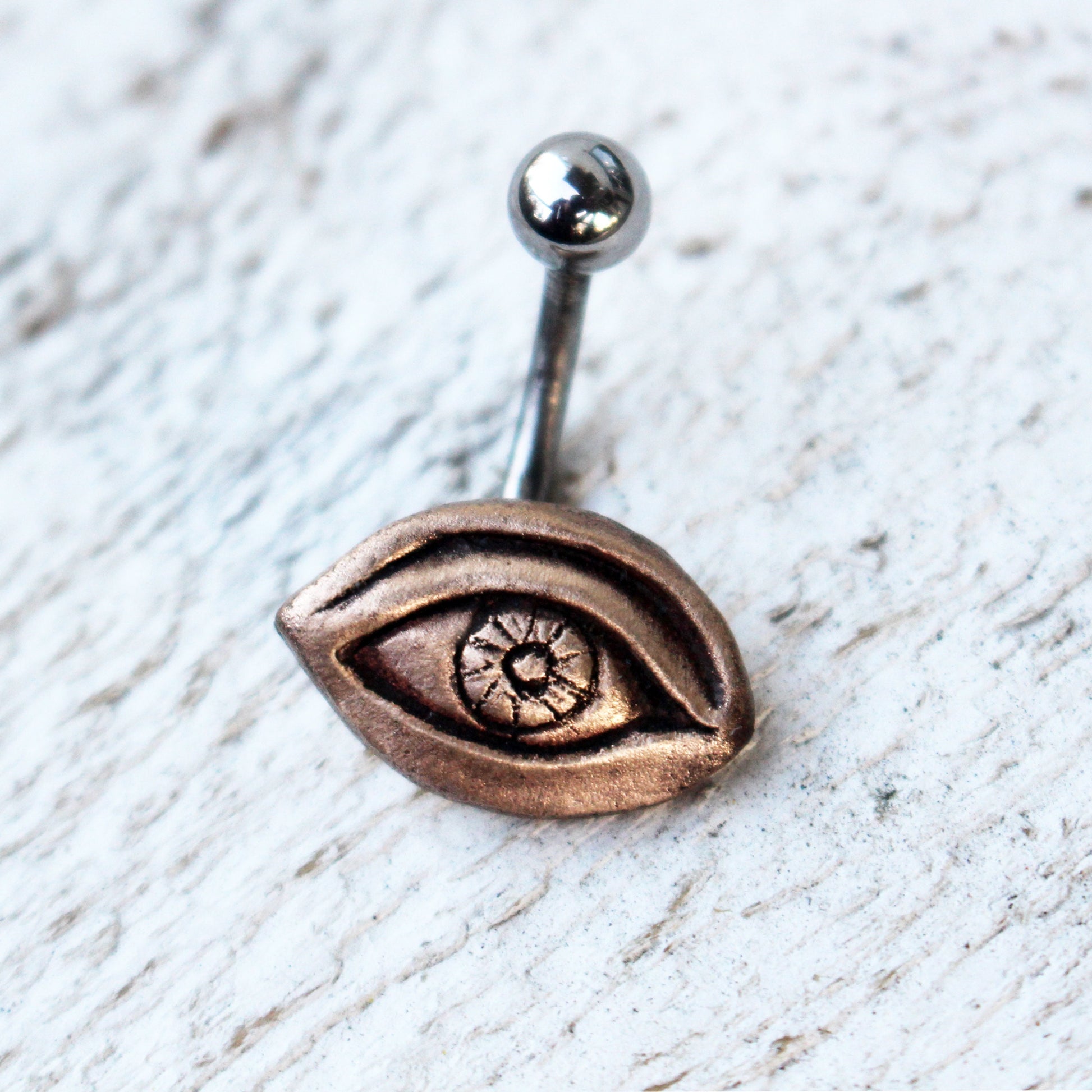A belly button ring with a bronze eye design attached to a titanium barbell.