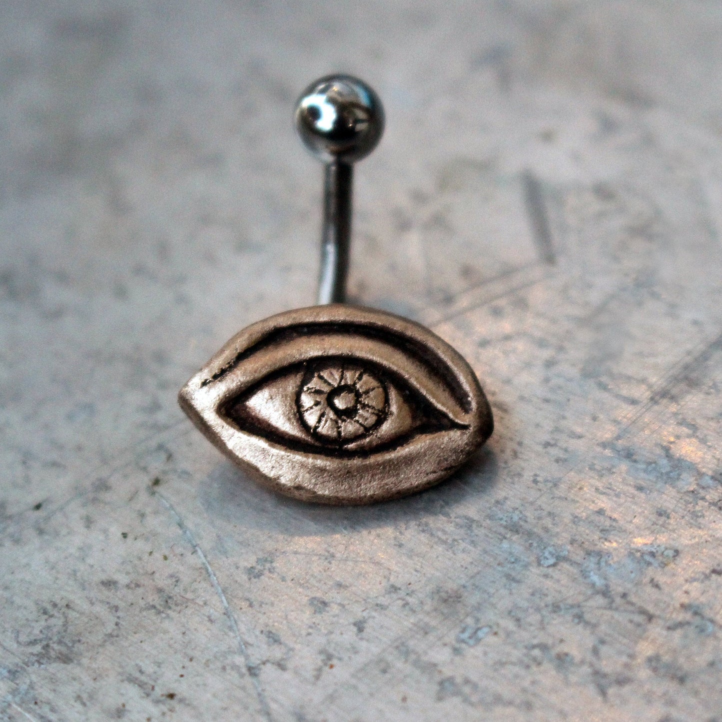 A belly button ring with a bronze eye design attached to a curved barbell.