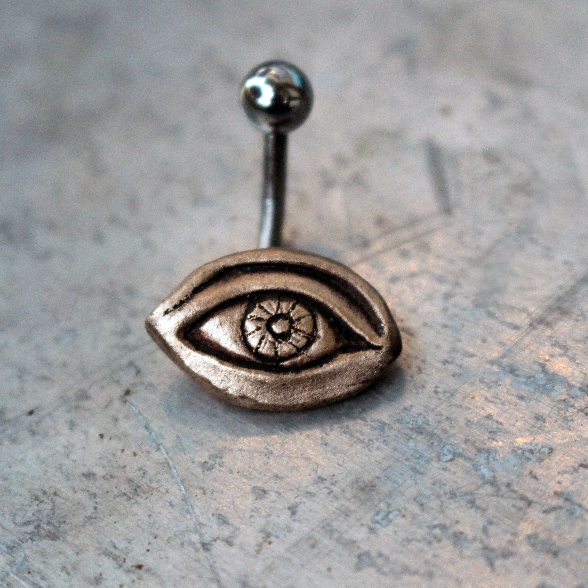 A belly button ring with a bronze eye design attached to a curved barbell.