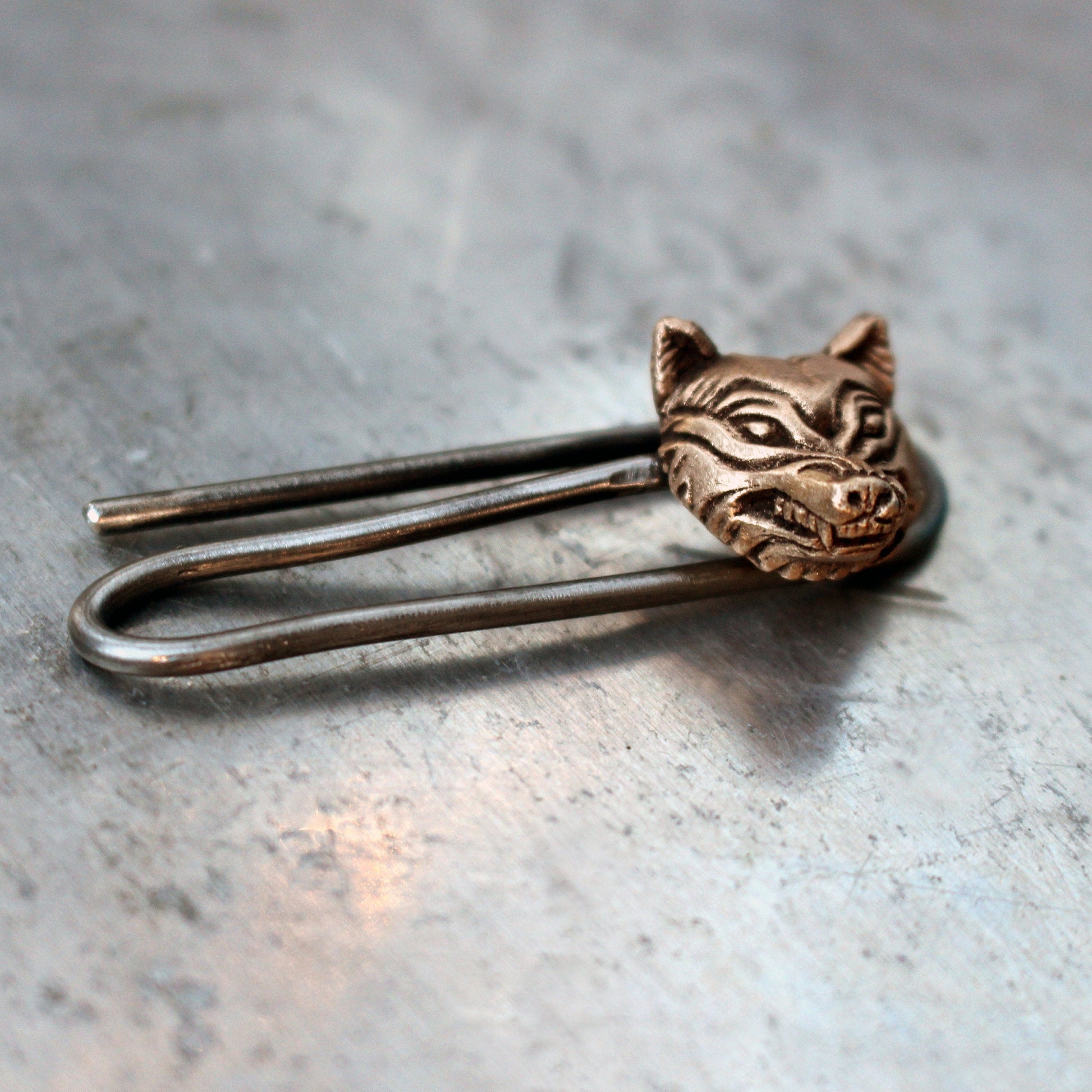 A tie clip with a bronze wolf head sculpted on it, with a stainless steel body.