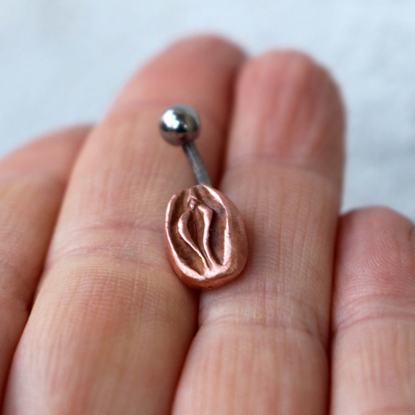 a belly button ring with a copper sculptural design representing a vagina