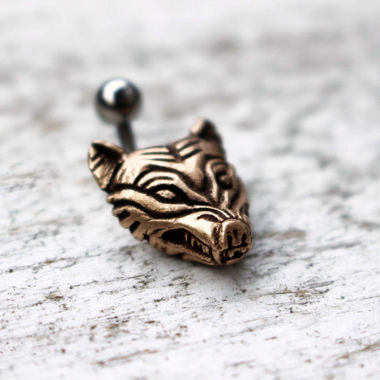 A bronze wolf head belly ring piercing with a surgical steel barbell.