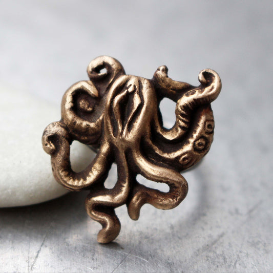 This image features a unique and artistic ring known as the "Mature octopussy ring, labia art." It showcases a bronze sculpture of an octopus creature with swirling tentacles, crafted with meticulous detail.