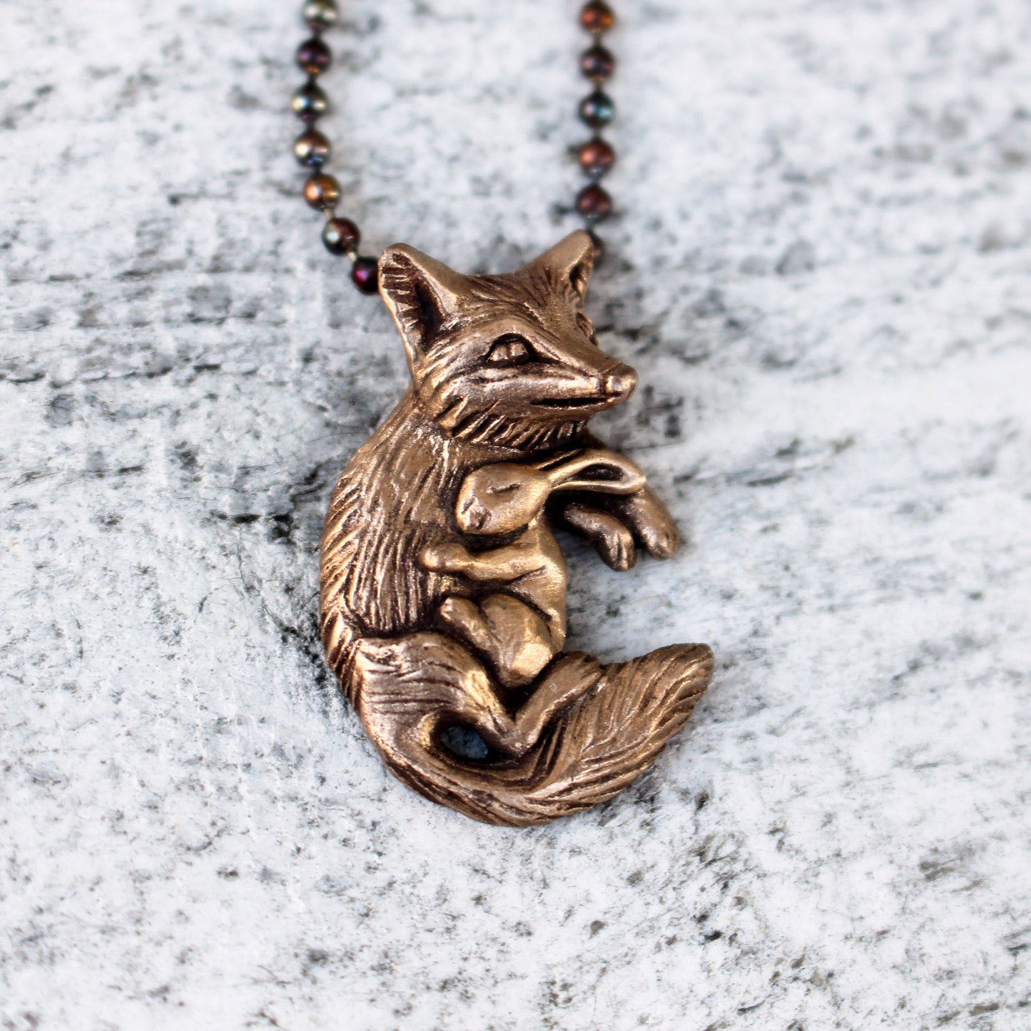 Bronze necklace featuring a sculpted fox and rabbit attached to a chain.