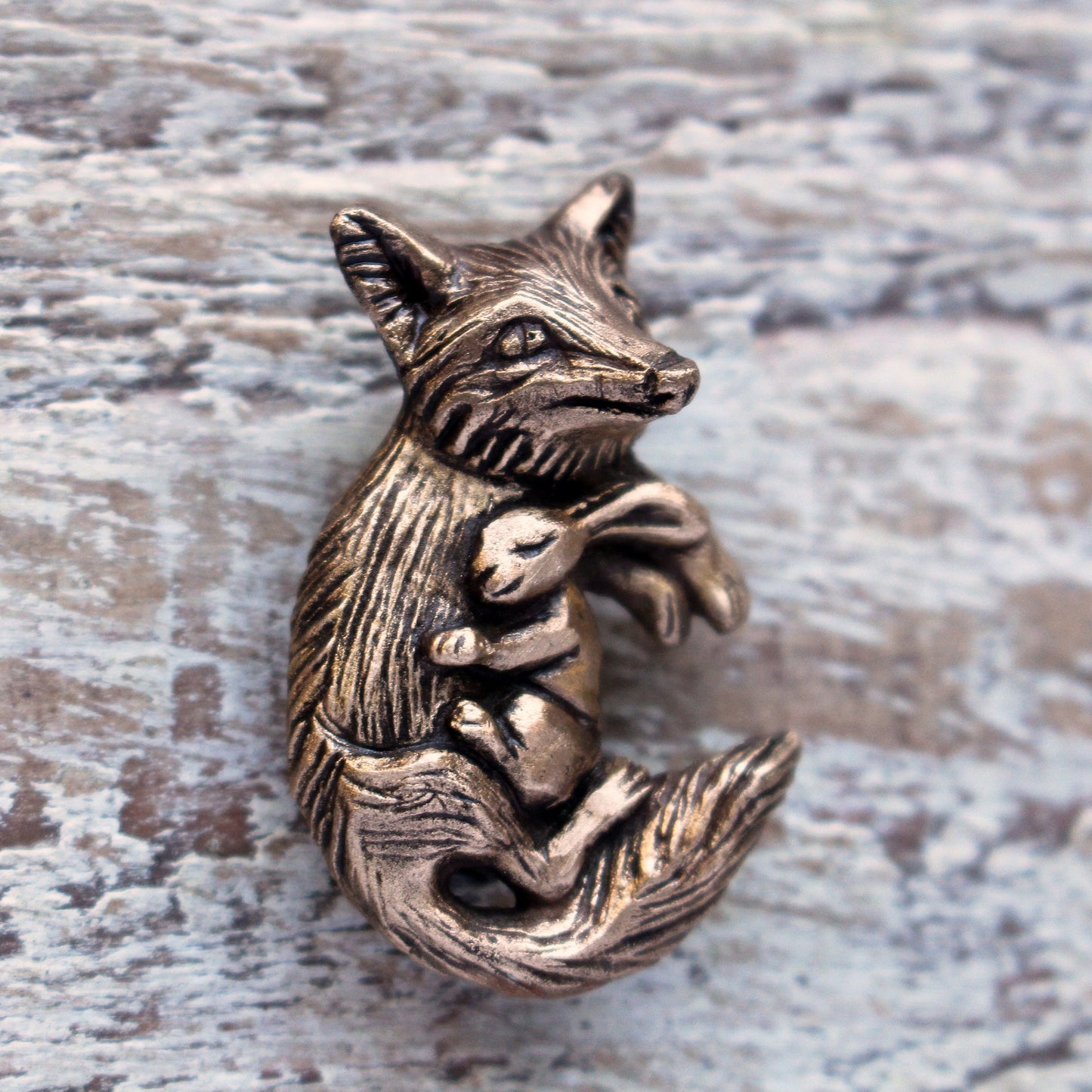 A bronze brooch in the shape of a fox and rabbit cuddling.