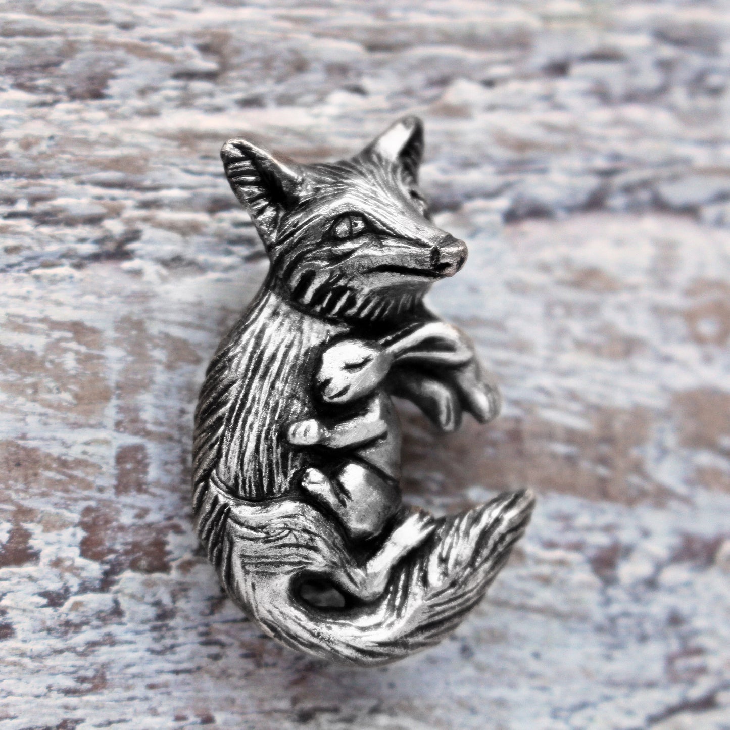 A silver necklace featuring a detailed fox and rabbit charm, displayed against a wooden background.