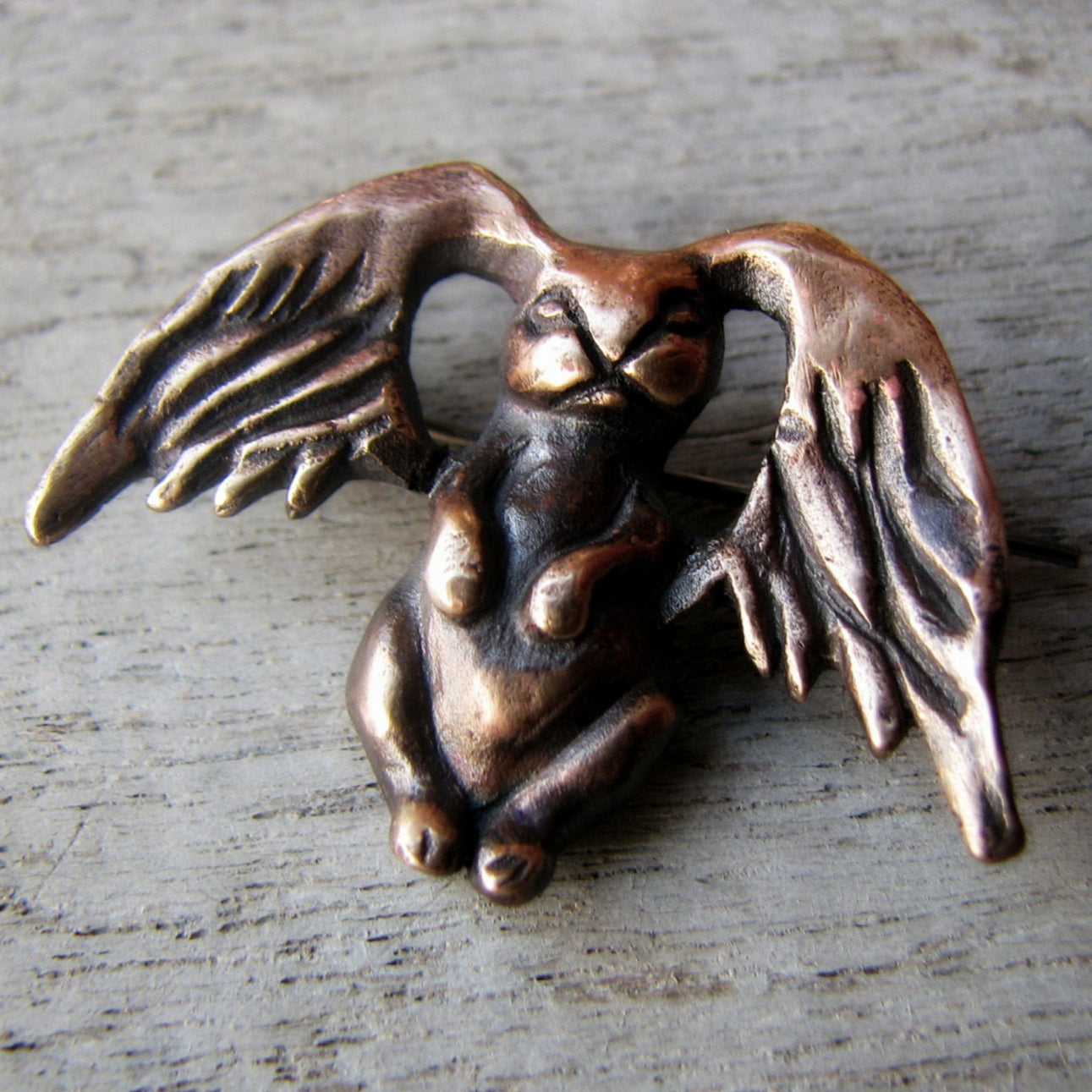 A bronze brooch in the shape of a winged bunny rabbit, with the brooch pin on the underside.