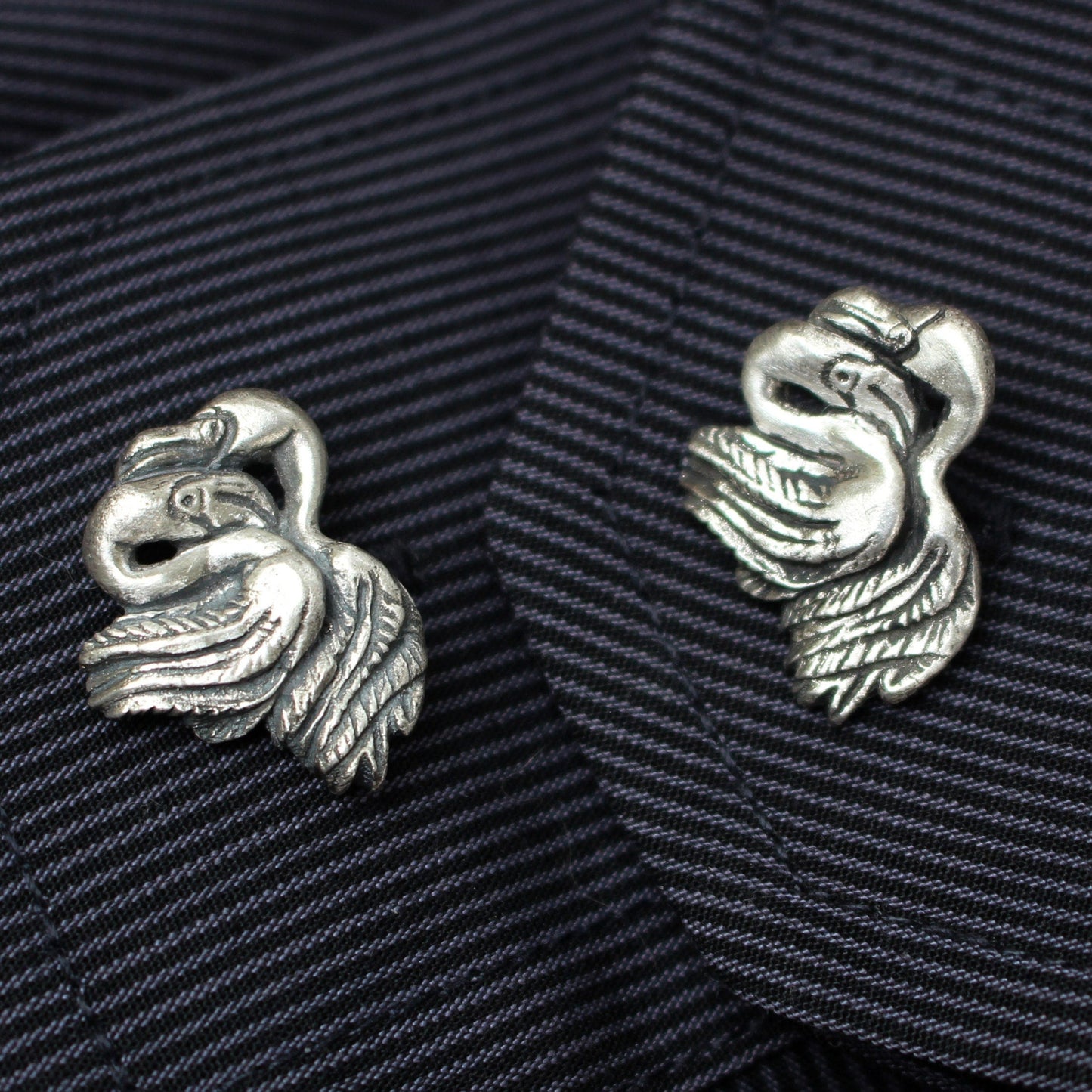 A pair of silver flamingo cufflinks on a striped fabric background.