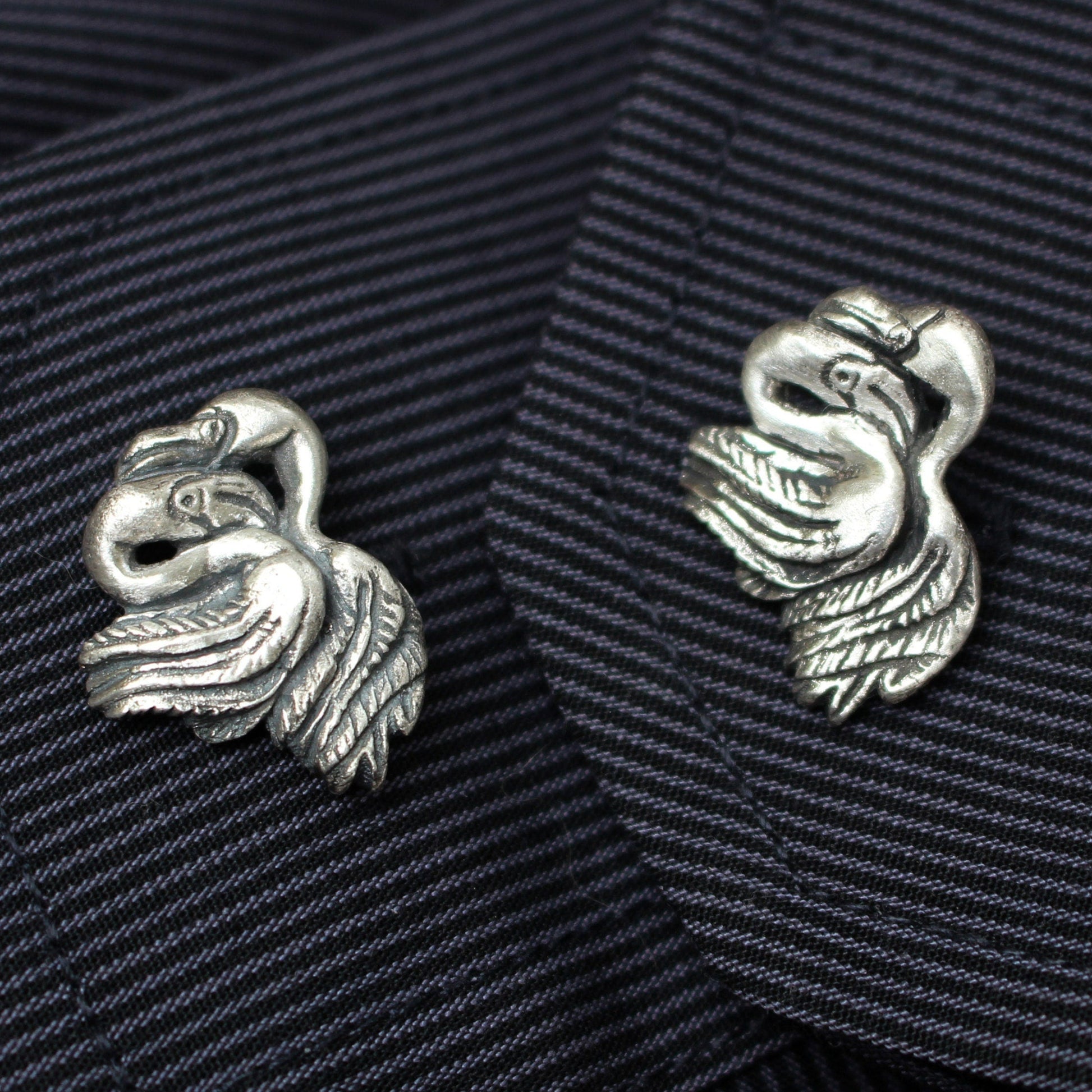 A pair of silver flamingo cufflinks on a striped fabric background.