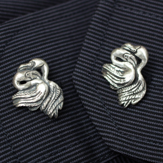 A pair of silver flamingo cufflinks on a striped fabric background.