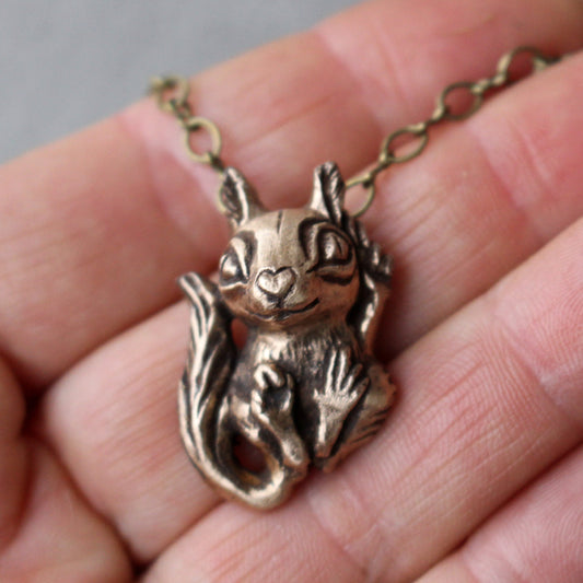 A small bronze squirrel necklace, with the squirrel sculpted with a heart-shaped snout and a tiny paw making a peace sign.