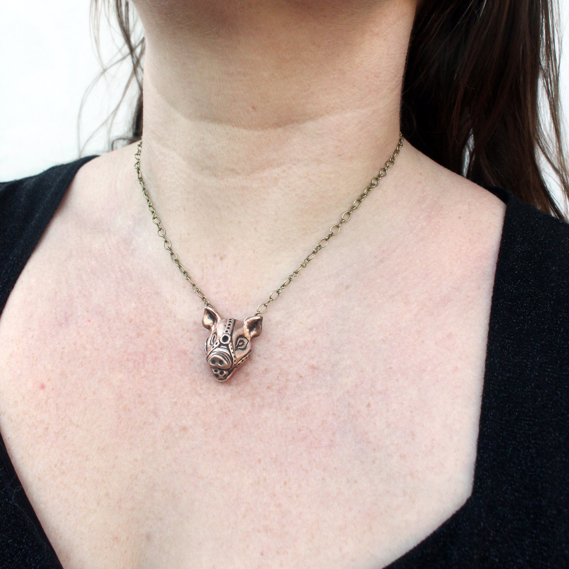 A bronze and copper pendant with kinky pig with a ball gag harness