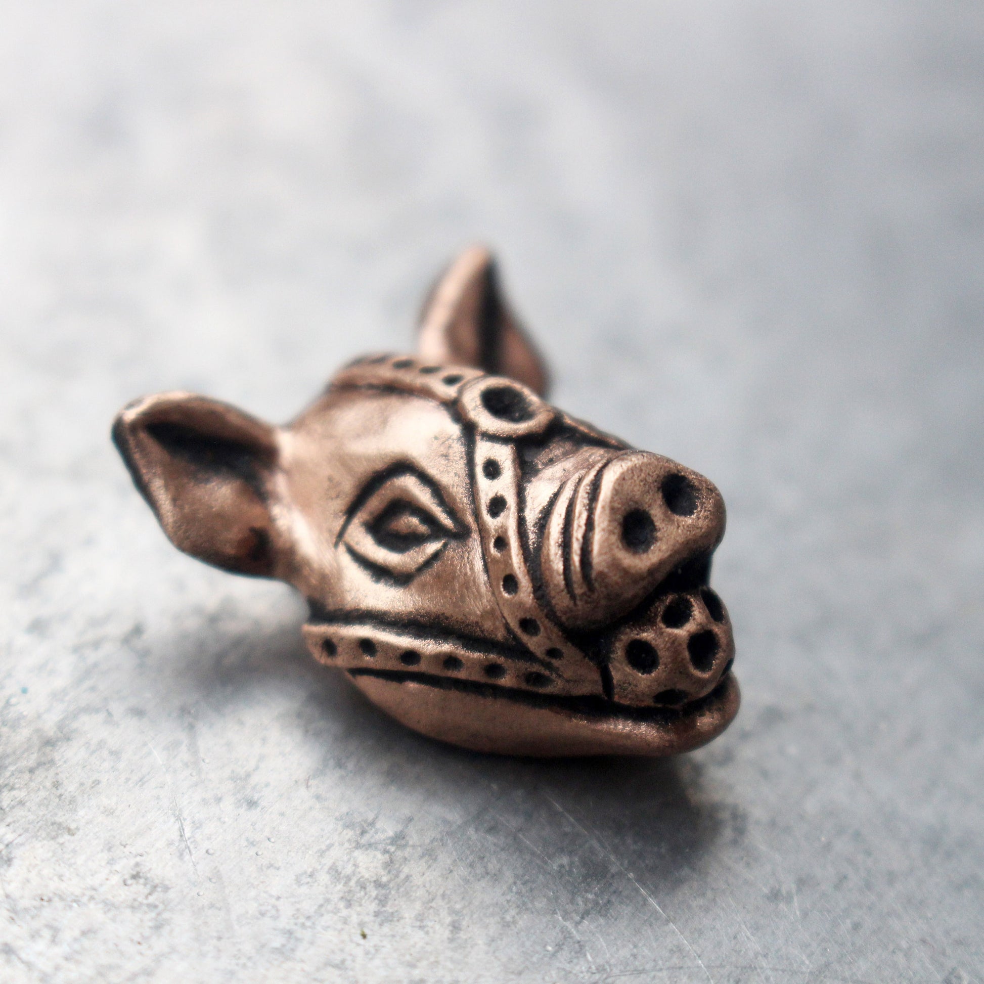 A bronze and copper pendant in the shape of a stylized pig with a ball gag harness.
