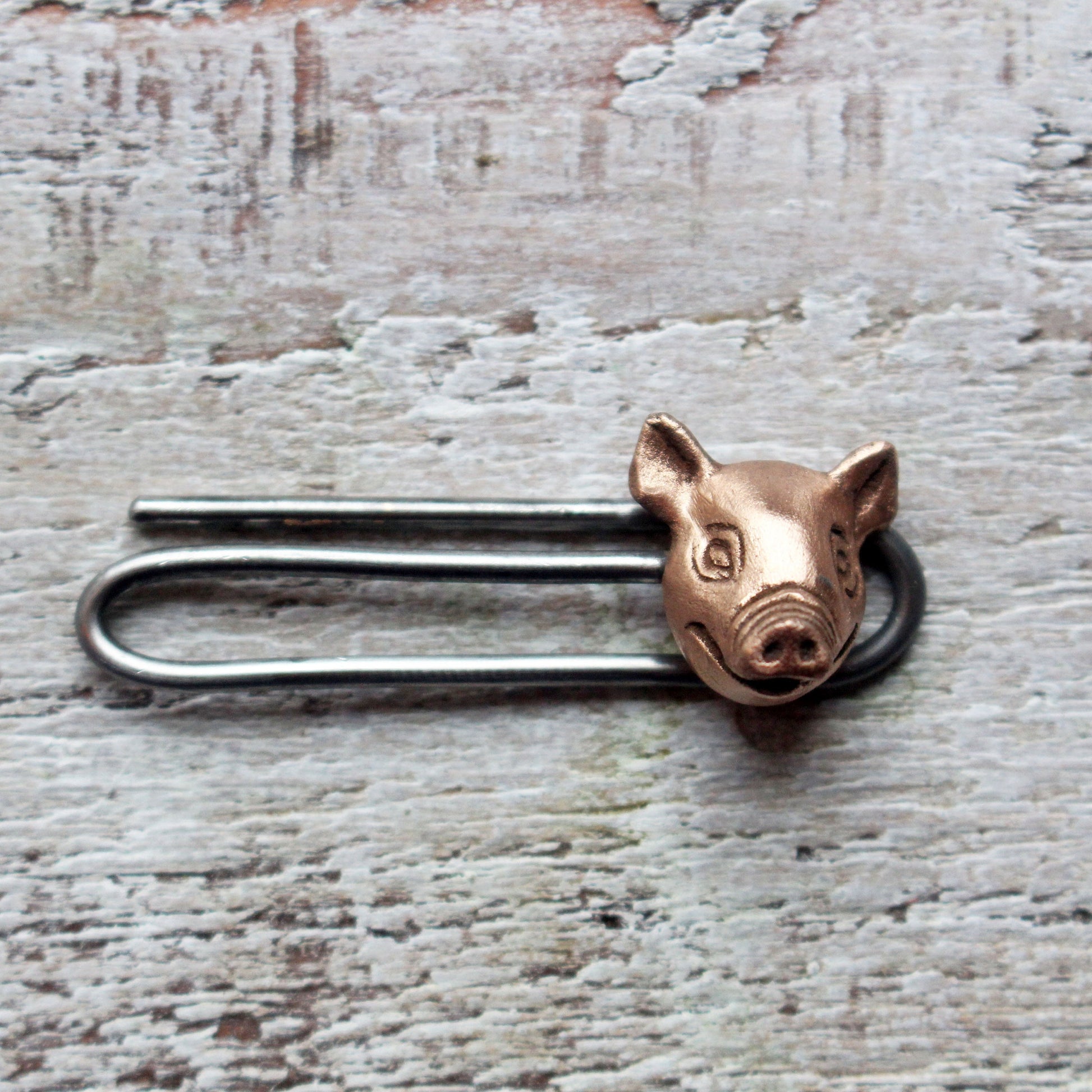 A tie clip with a pig head design, made in copper with a stainless steel pin
