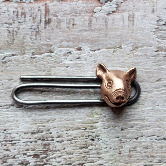 A tie clip with a pig head design, made in copper with a stainless steel pin