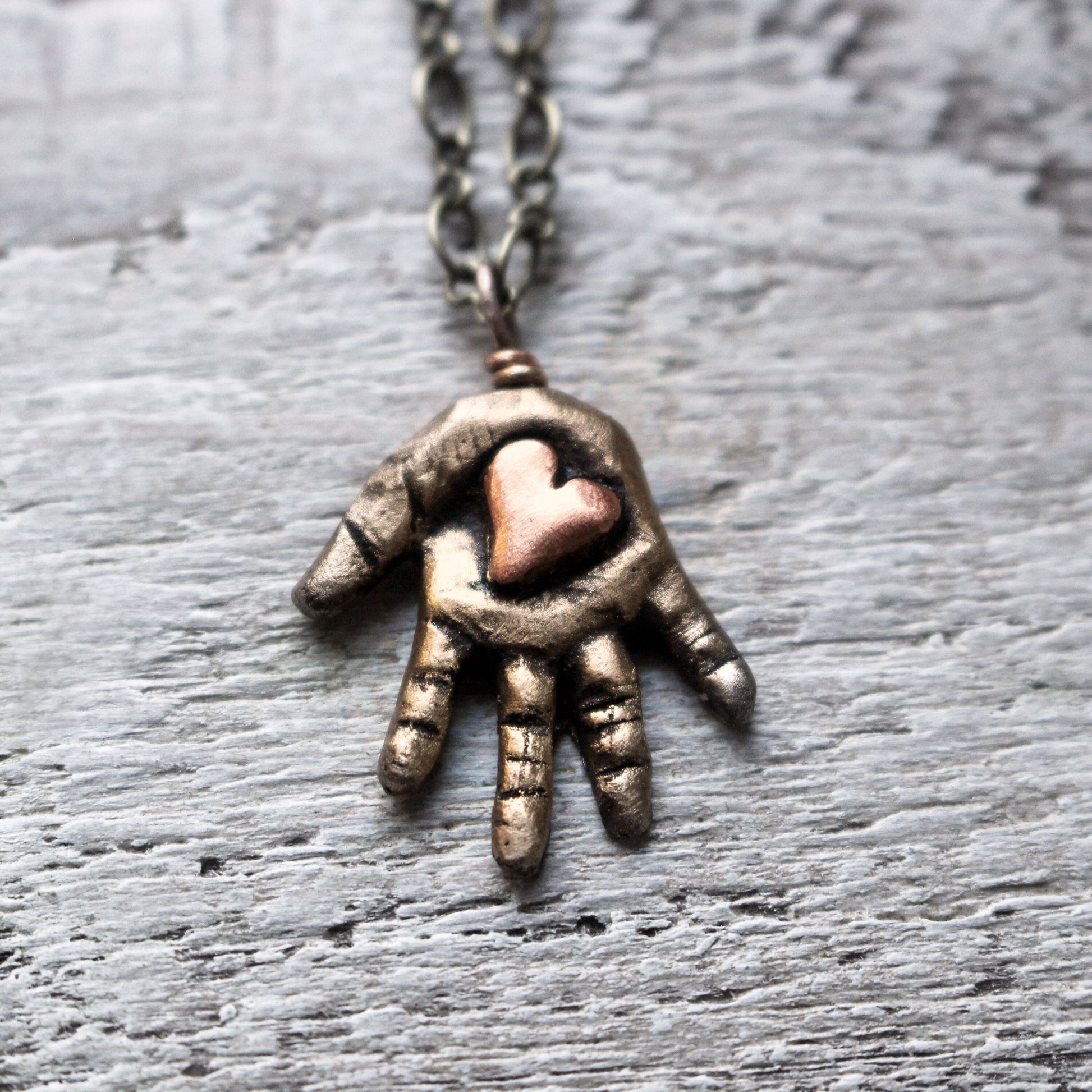 Bronze hand-shaped pendant with a pink copper heart in the palm