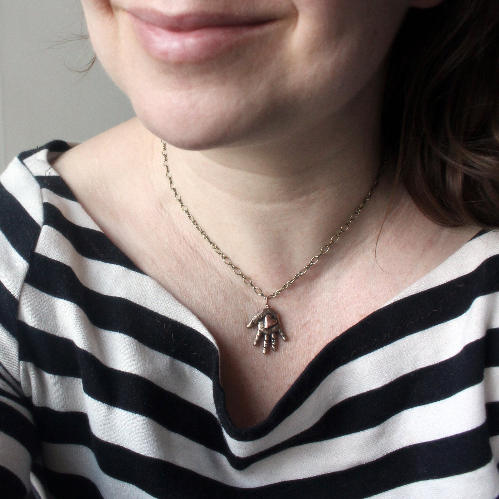 Bronze hand-shaped pendant with a pink copper heart in the palm