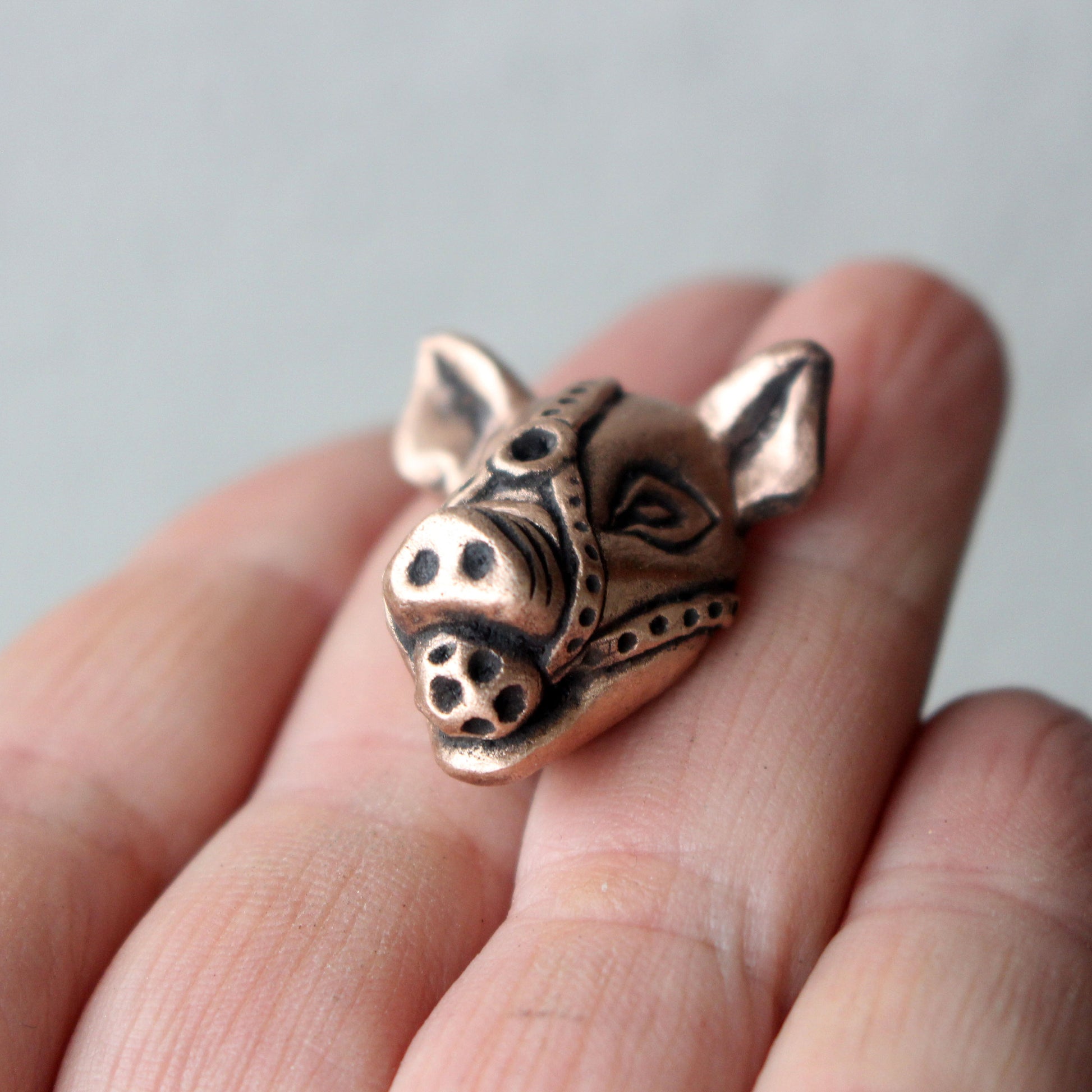 A bronze and copper pendant with kinky pig with a ball gag harness