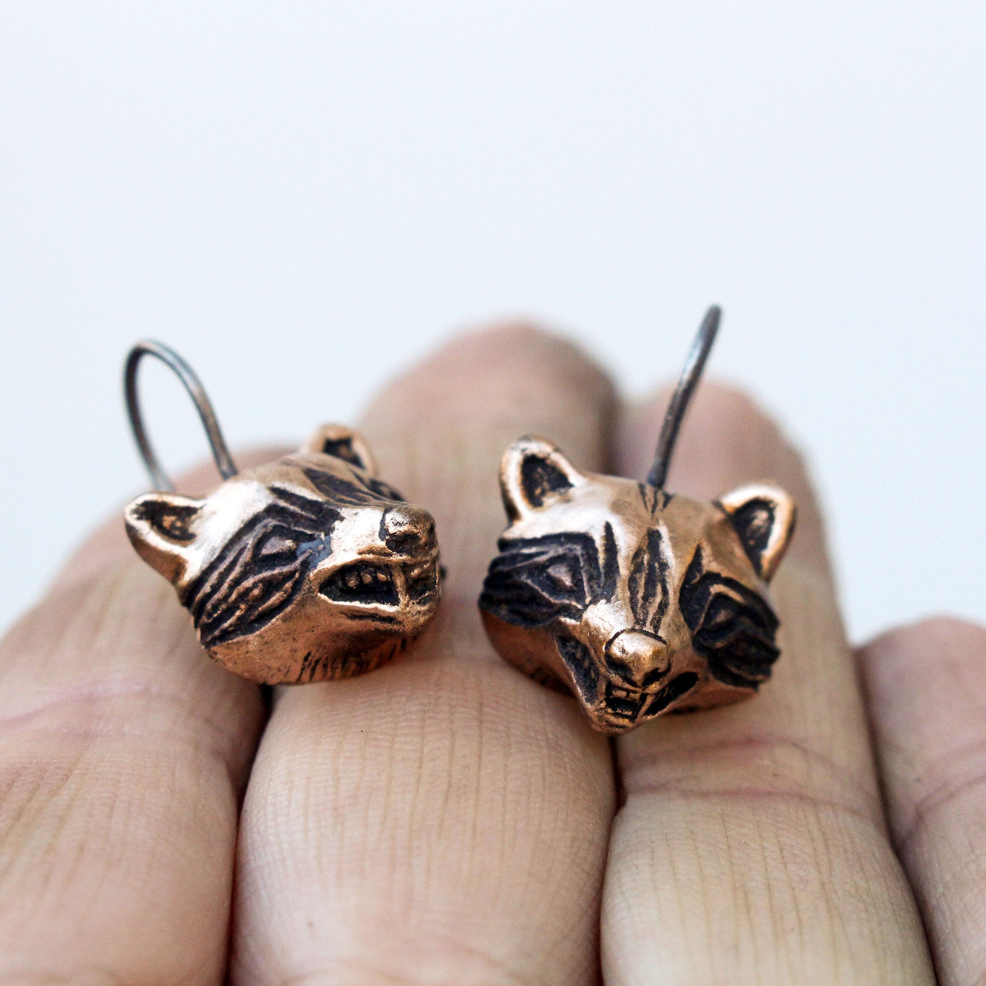 A pair of handmade dangling raccoon earrings made of bronze and titanium