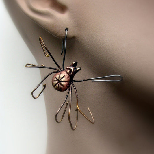 A bronze and silver spider earring with intricate detailing on a person's ear,