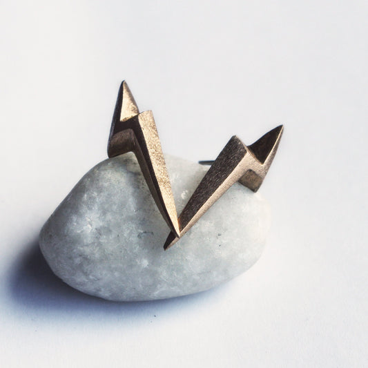 A pair of bronze lightning bolt earrings placed on a white stone.