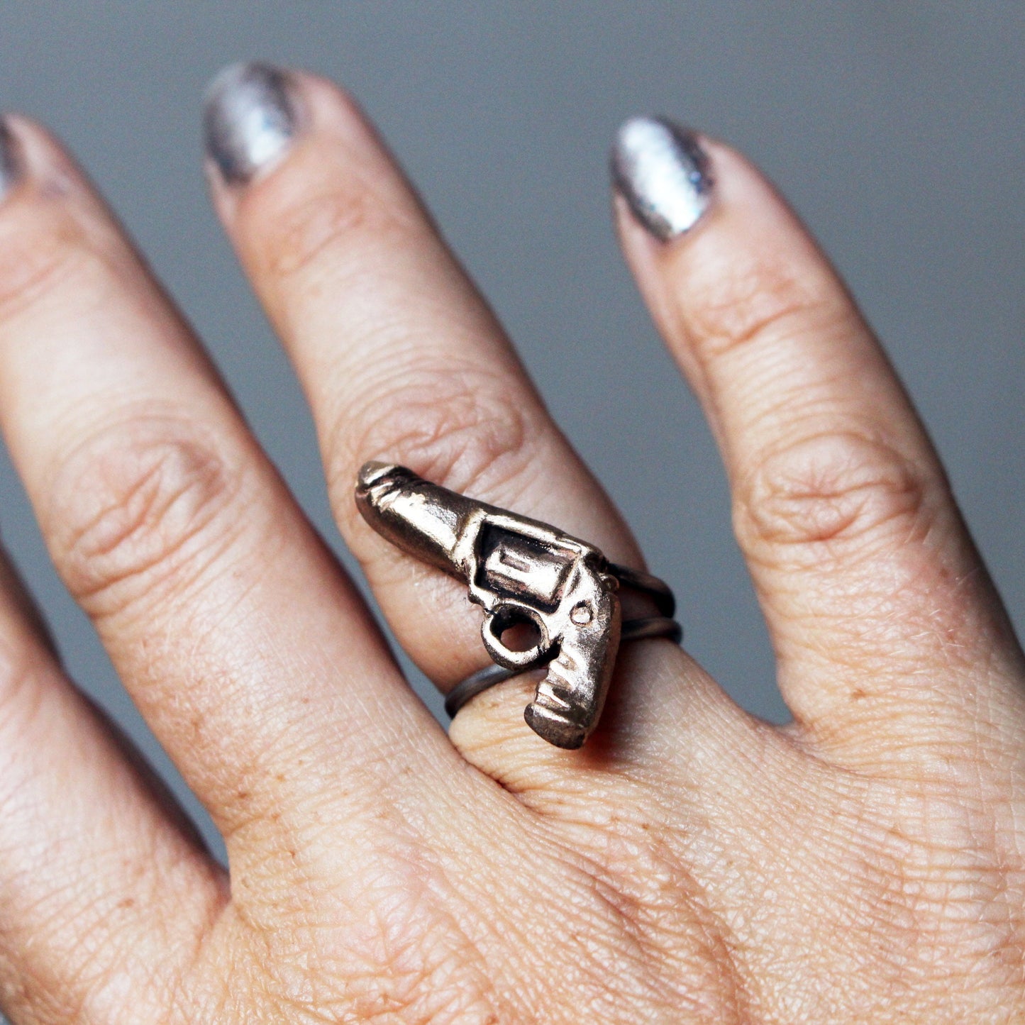 A bronze-colored ring with a sculpted penis gun design on a person's hand.