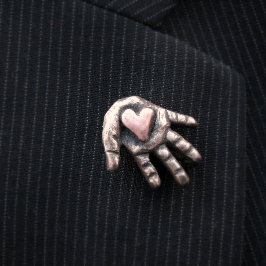 Metallic hand-shaped brooch with a pink heart