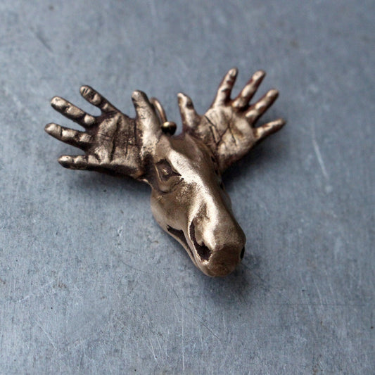 Bronze moose head pendant with antlers extended in a surreal style, placed on a metallic surface.