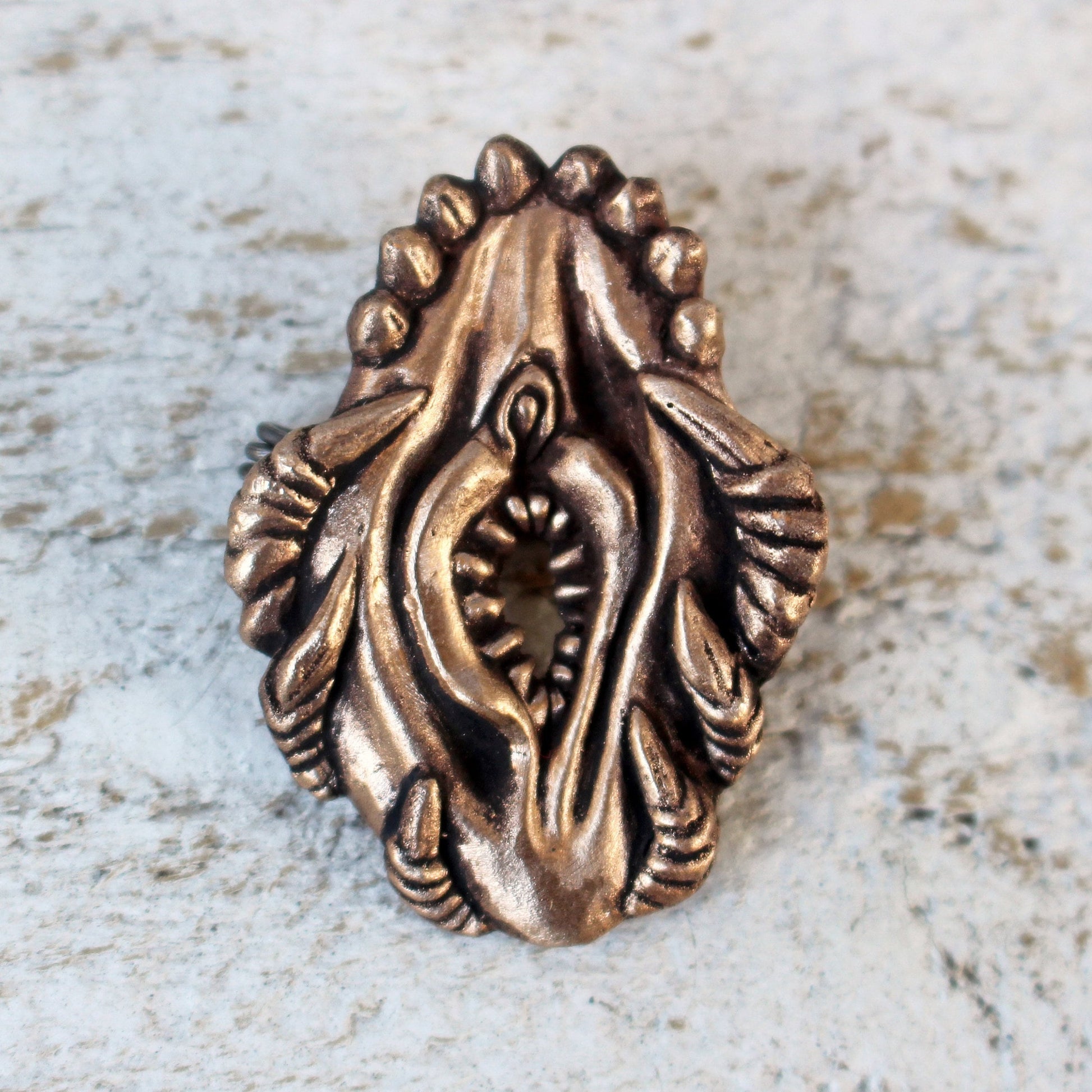 bronze brooch sculpted in the shape of a stylized female genitalia, with fangs and claws