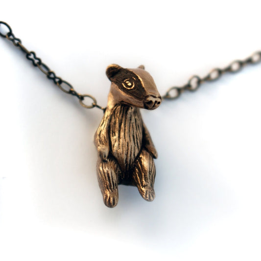 A bronze pendant in the shape of a small badger, with a textured body and a chain attached to its top.