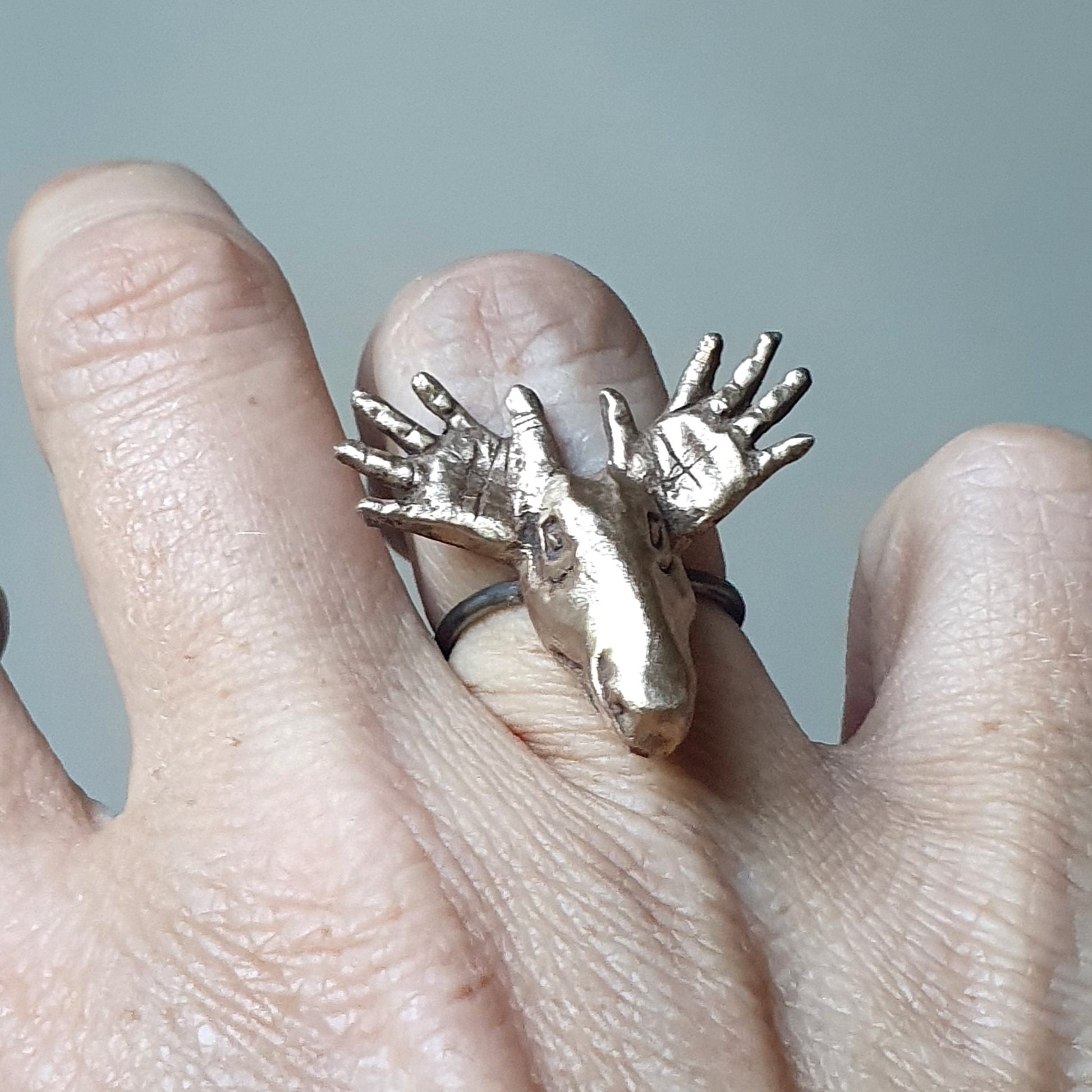 A bronze moose head ring with an adjustable ring shank, displayed on a person's finger.
