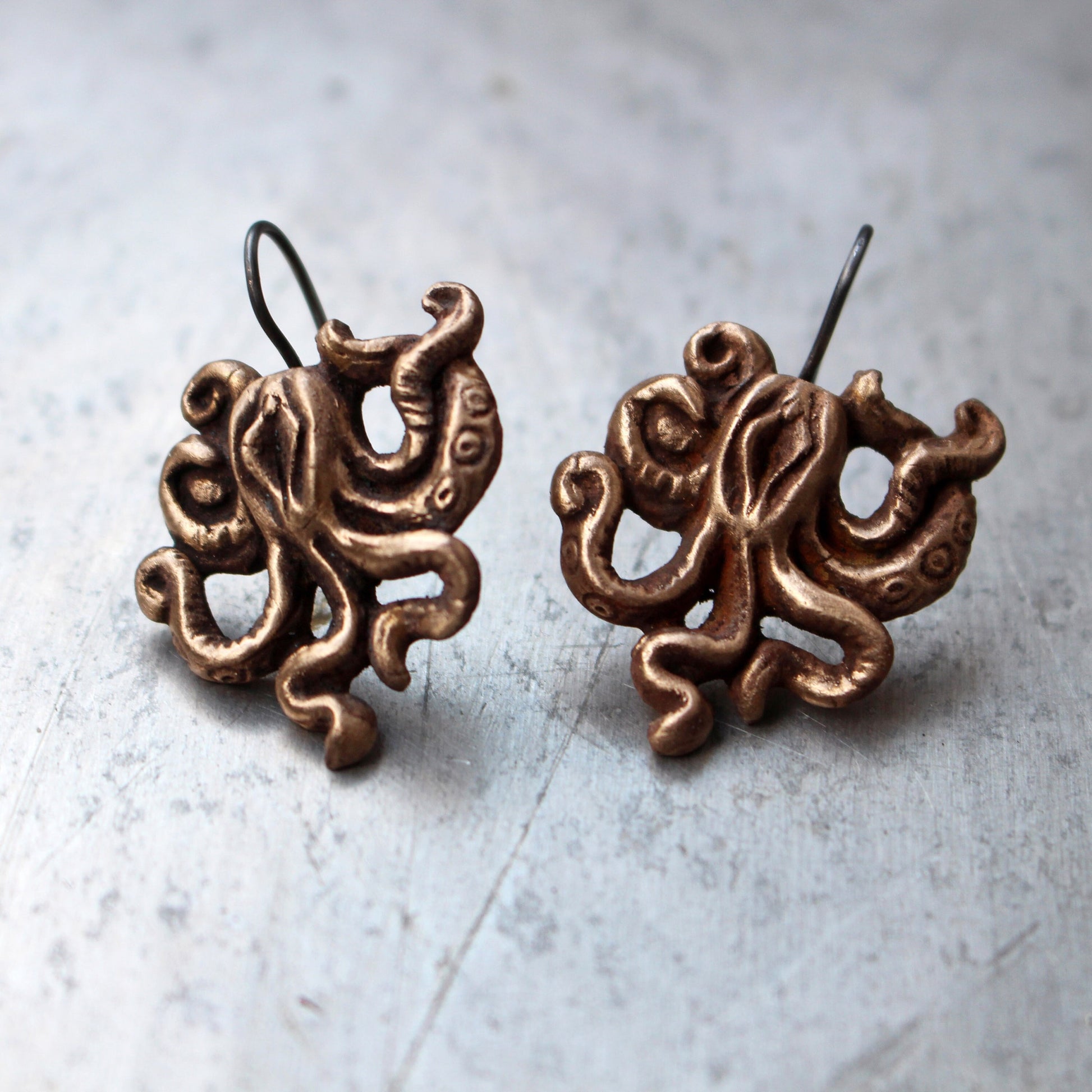 This image displays a pair of distinctive earrings shaped like mature, tentacled monsters, reminiscent of an octopus. These earrings are intricately crafted from bronze, showcasing detailed sculpting that enhances their quirky and artistic appeal.