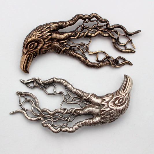 Two bird head pendants with intricate filigree designs, one in a silvery appearance and the other in a bronze hue, against a white background.