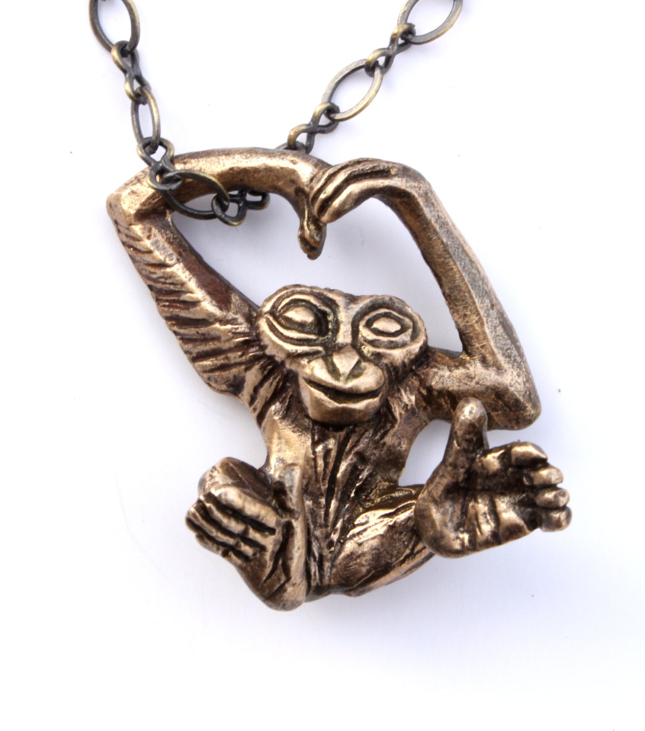 A silver necklace with a detailed miniature sculpture of a monkey swinging in the chain, crafted with focus on the monkey's feet and hands.