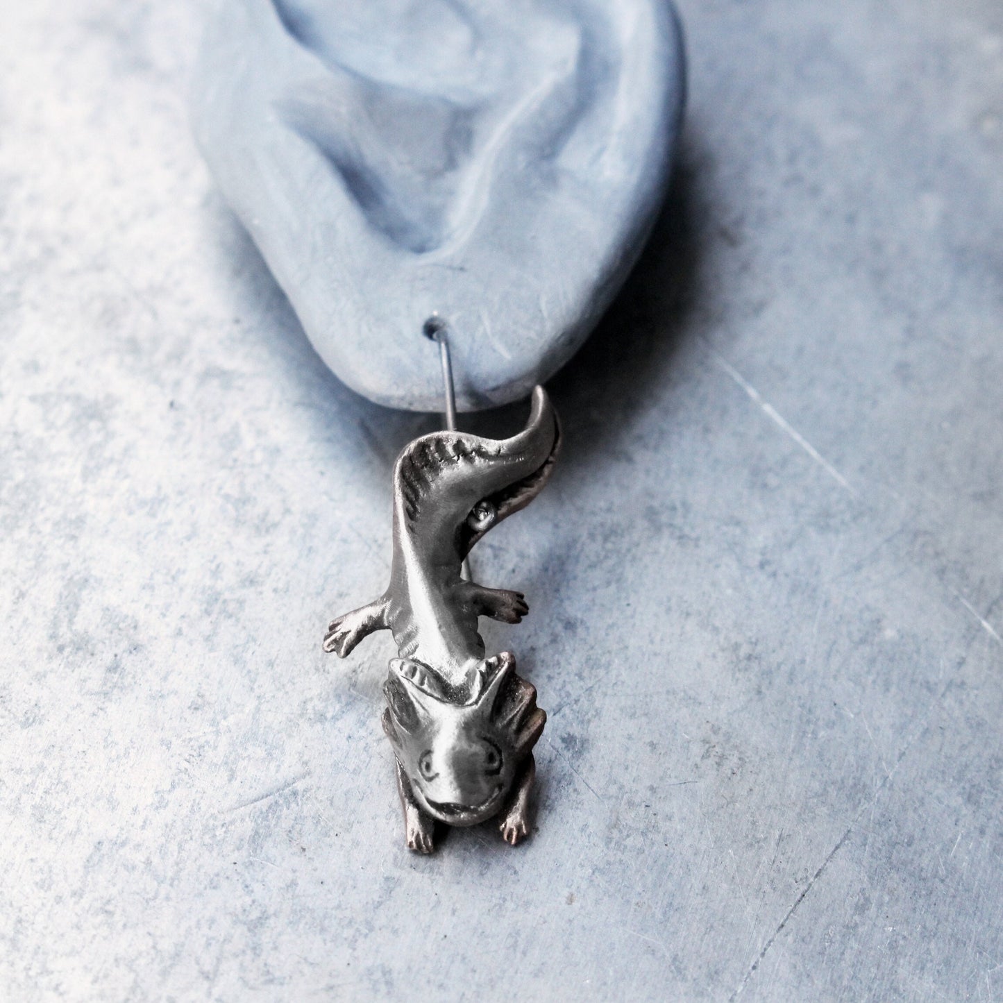 handgjort axolotl örhänge i sterlingsilver hänger från ett keramik öra