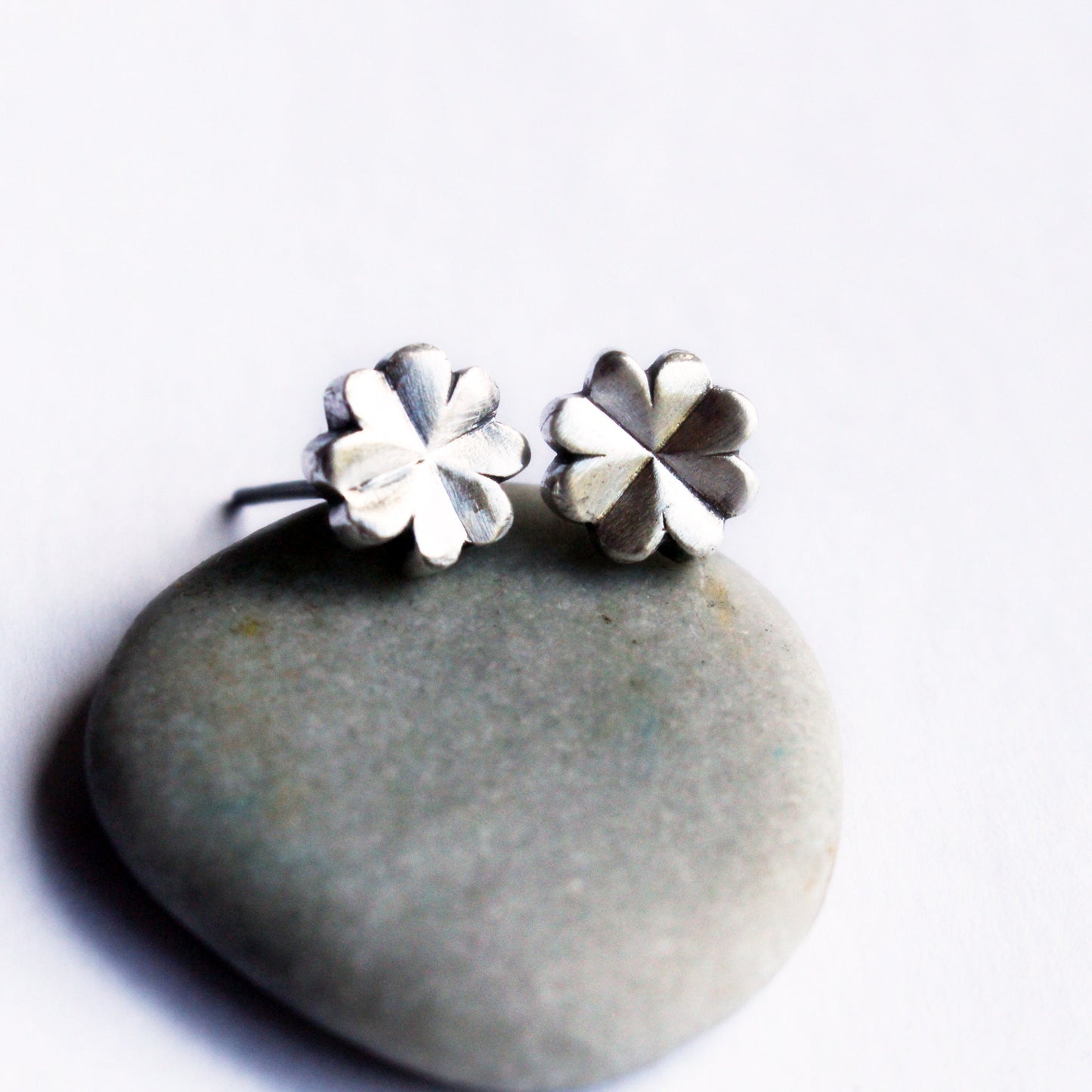 A pair of silver clover-shaped earrings placed on a stone.