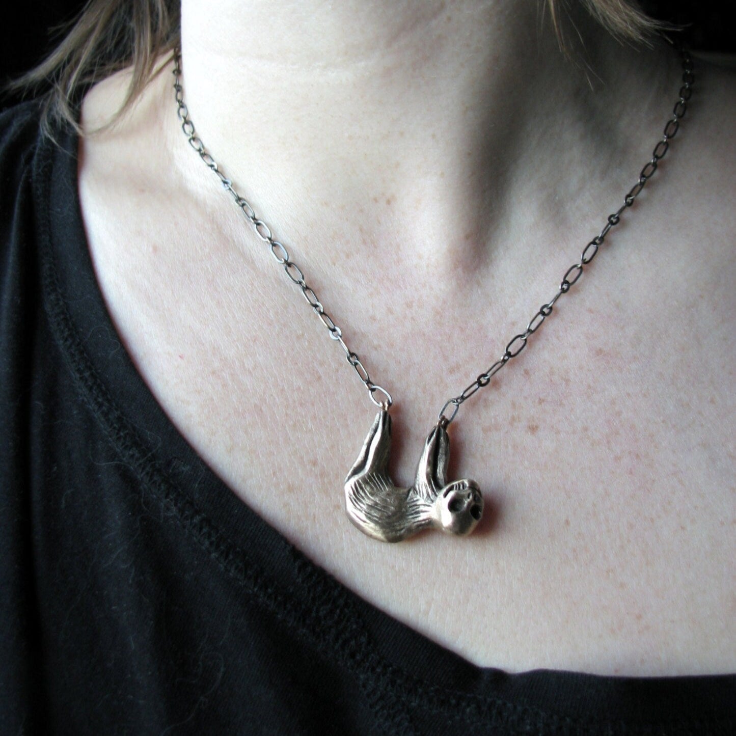necklace charm with a surreal sloth with a skull for face