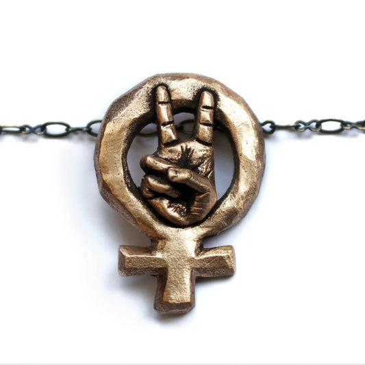 Feministsmycke i brons med en hand som gör v tecken