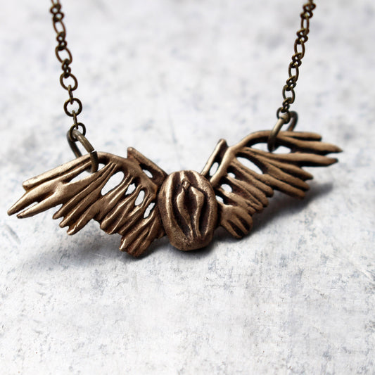 A bronze pendant in the shape of a winged vagina, attached to a chain necklace.