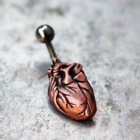 A belly button ring featuring a pink copper anatomical heart design.