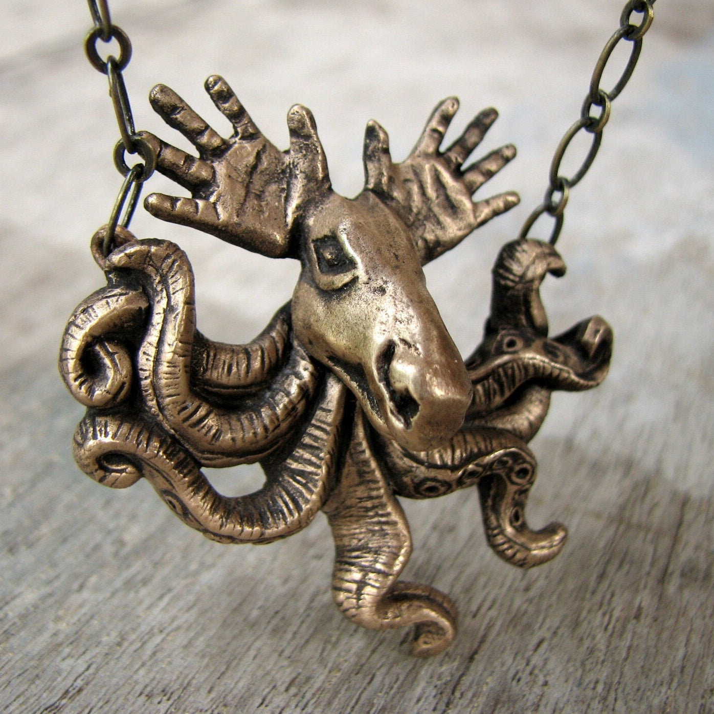 A bronze pendant featuring a surreal creature with tentacles and antlers, resembling a moose with hands as antlers